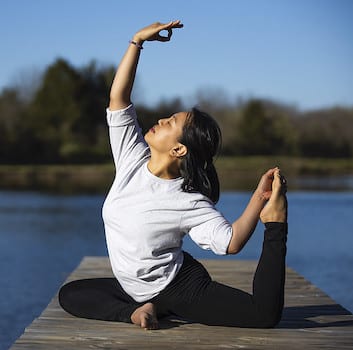 Woman in pigeon pose on a dock with lake in the background.